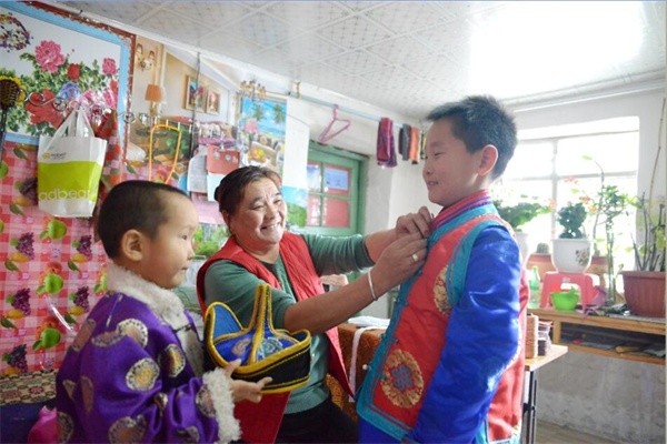 □2020年1月20日，和布克赛尔蒙古自治县莫特格乡哈拉尕特村村民科克玛尼吉·乌加，给邻居家两个小孩试穿她缝制的蒙古族服饰，送去新春的祝福。