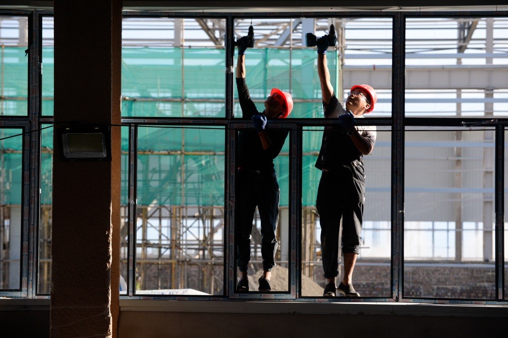 □工人在安装试验区风机叶片制造项目内的门窗。